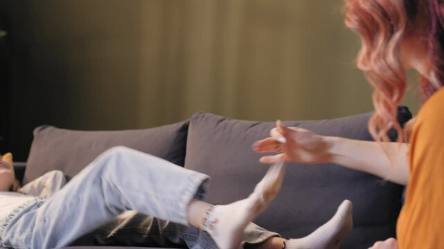 Mother taking off socks from daughter lying on sofa at home