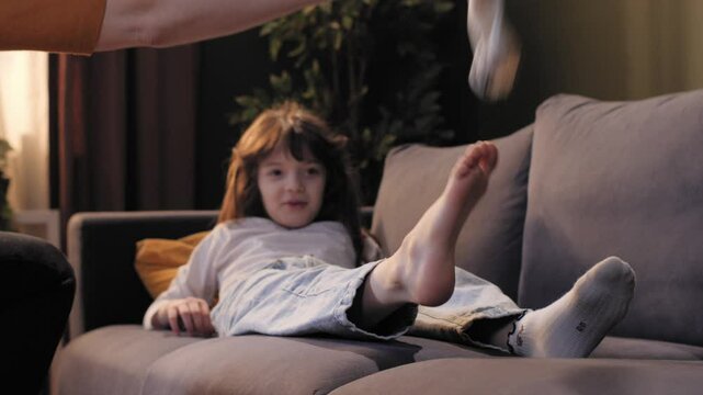 Mother taking off socks from daughter lying on sofa at home