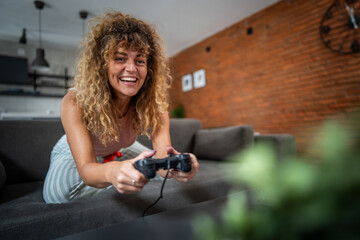 Excited woman playing videogames at home on the couch © Migma_Agency