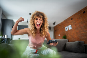 Excited woman winning at video game and showing strength at home © Migma_Agency