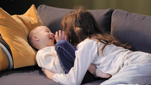 Sister tickling brother on sofa, having fun