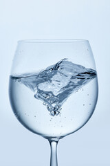 Close-up photo of water swirling in clear stemmed glass, showing movement and bubbles, against minimalistic background. Mock up. Concept of nutrition and hydration, drink, beverage. Ad