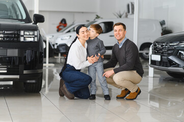 Happy parents with small kid after receiving keys for their new car in a showroom