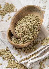 Wooden bowls full of dried green lentils on white table top view. Traditional mediterranean legume