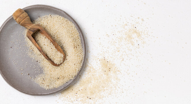 Raw uncooked fonio seeds on grey plate with a wooden scoop on white table topview. African cereal