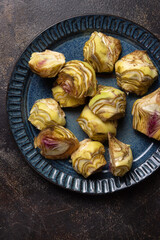 Plate full of fresh raw artichoke hearts ready to cook on dark rustic table top view, copy space