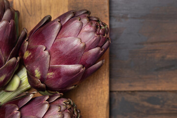 Whole purple raw roman artichokes on a dark wooden table top view. Fresh italian vegetables