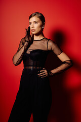 Elegant young woman exudes confidence in chic attire against a vibrant red backdrop