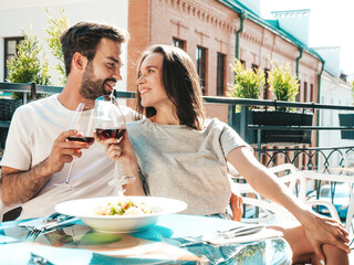 Smiling beautiful woman and her handsome boyfriend. Happy cheerful family. Couple cheering with glasses of red wine at their date in restaurant. They drinking alcohol at veranda cafe in the street
