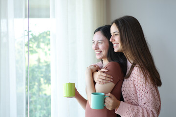 Happy interracial lesbian couple drinking and looking through a window