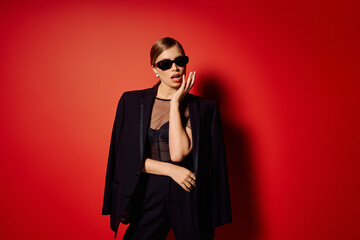 Elegance personified in a chic black outfit against a vibrant red backdrop