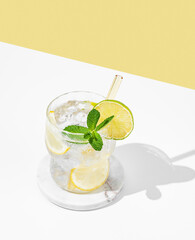 Cocktail mojito with lime, lemon, mint and ice in a glass on a white yellow background with shadow.