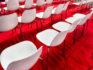 Rows of empty white chairs arranged on a vibrant red carpet for an upcoming event at a convention...