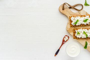 Crispy toasts with farm cottage cheese on wooden board, top view