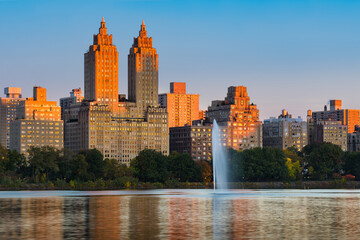 Obraz premium Sunrise on Upper West Side high-rise buildings and Jacqueline Kennedy Onassis Reservoir fountain in Central Park. Manhattan, New York City