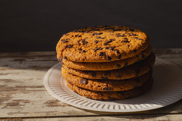 A solitary chocolate cookie at the center of the composition. The image represents a quiet break for tea or coffee. Homemade baking against a backdrop of bright sunlight.