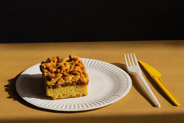 Homemade jam and crumb cake on a white plate, accompanied by a disposable knife and fork in bright sunlight. Quick preparation of homemade food and a calorie-rich dessert for a picnic.