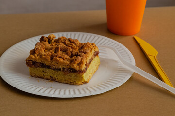A white plate on a yellow-sandy background with a golden-brown homemade pie with jam and crumbs. A symbol of comfort food, calorie-richness, and recipes for homemade baking.