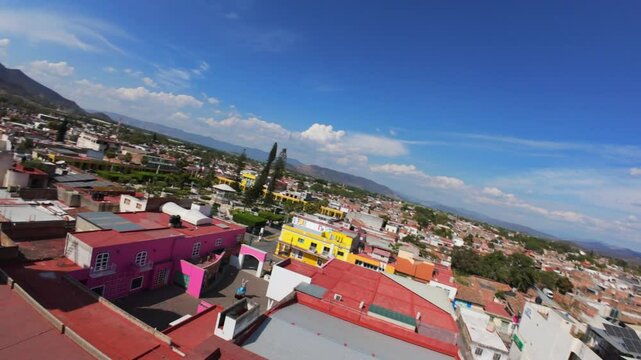 Drone shot capturing the detailed architecture of a historic church dome in Tuxpan, Jalisco, Mexico. The view extends over the city with rolling mountains in the background under a vivid blue sky.