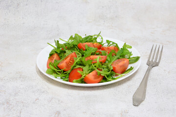 Fresh and Healthy Arugula and Tomato Salad on a White Plate with a fork