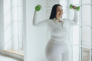 Big fat large woman model in sportswear doing sports on yoga and pilates mat ready for workout in home fitness gym.