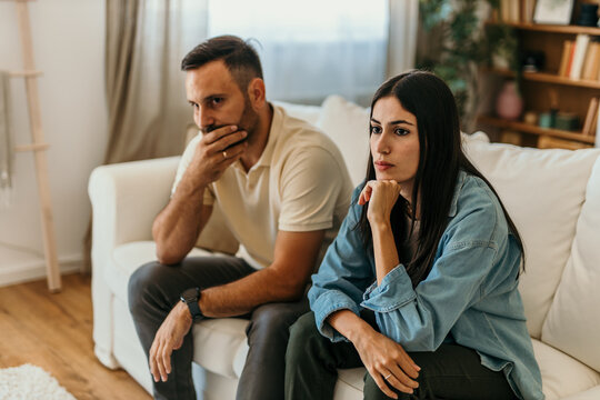 Worried couple sitting on sofa thinking about problems in relationship