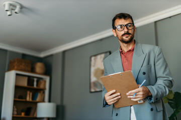 Building inspector wearing glasses and holding clipboard inspecting house