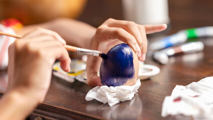 Obraz premium A little girl is painting on an egg with a paintbrush for easter egg decoration on the table. Concept of celebrating the easter holiday