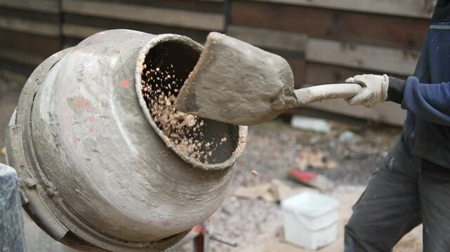 Worker Adding Sand to Concrete Mixer on a Building Construction Site