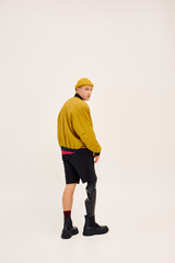 Young man confidently showcases stylish outfit with prosthetic leg in modern studio