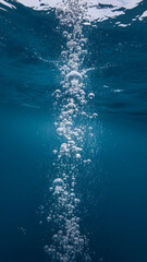 Fototapeta premium Underwater scene showing numerous air bubbles rising in a dark blue ocean, creating a vertical stream of light and airy texture symbolizing purity, freshness, and underwater life