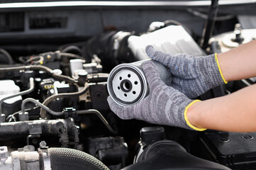 Auto mechanic is replacing fuel filter. Man holds diesel fuel filter in hands against engine compartment background, close-up. Auto parts replacement concept.