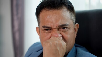 Irritated businessman is covering his nose and making a disgusted expression