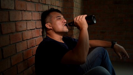 Asian Man sits alone at home looking sad and distraught and Drinking from Bottle