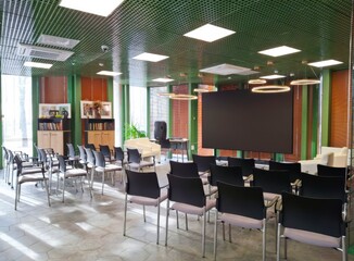 An empty, bright conference room with wide windows, chairs and a large screen