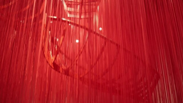 Abstract red thread installation with a skeletal boat structure subtly visible behind cascading strands. A mesmerizing and immersive background, perfect for artistic or conceptual video projects.