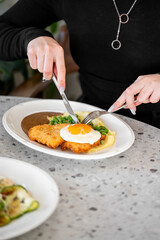 A close-up of a person enjoying a delicious meal of crispy chicken, mashed potatoes, and a sunny-side-up egg, captured in a cozy dining setting.