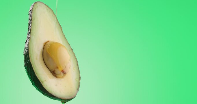 side view of slice of avocado fruit with seed soaked in fresh natural oil pouring down from it