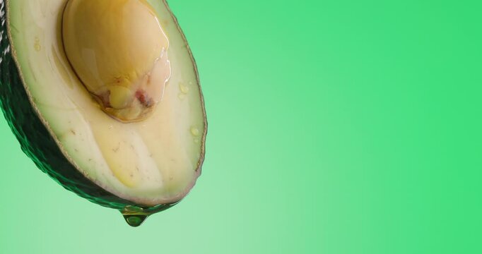 closeup of raw avocado oil pouring down from its fruit in slow motion on green background