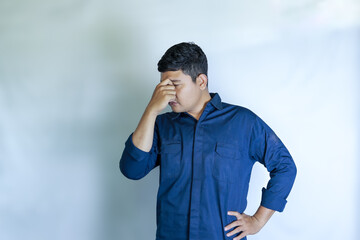 young asian man in blue shirt holding head with hands, his face showing pain expression, headache with white studio background. Concept of disease