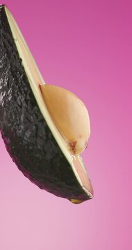 side view of a slice of avocado with fresh juice pouring down from it on pink background