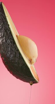 sde view of fresh avocado cut in half with nutritious fatty oil coming from its seed on red background