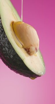 delicious avocado juice coming from freshly cut avocado fruit and pouring down on pink background