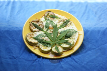 cannabis food. classic cannabis leaf lies on a fried egg baked with zucchini and marijuana leaves. grated cheese sprinkled on top. a plate of food lies on an old rustic window overlooking the garden