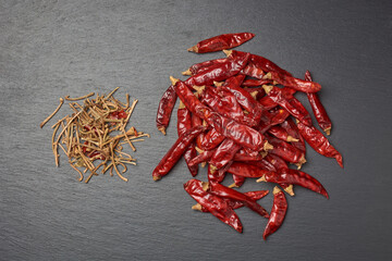 pile of dried chili peppers with stem cut off on black textured surface background, preparation step for making chili powder or flakes, taken from above