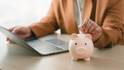 Financial savings and investment concept. Person inserting coin into piggy bank while working on...