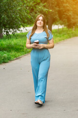 Happy woman with a coffee cup strolling in a vibrant park under sunlight, with green trees around. Great for wellness, leisure, and casual outdoor scenes.