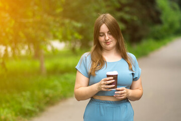 A woman with a coffee cup in a sunny park, surrounded by greenery and a serene path. Perfect for lifestyle, relaxation, and nature themes on a bright day