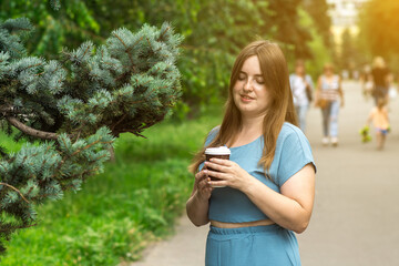 A woman enjoying a coffee in a lush park on a sunny day, surrounded by greenery and people strolling. Perfect for lifestyle, relaxation, and outdoor themes.