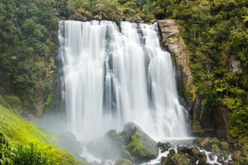 Fototapeta premium Stunning waterfall cascades down lush green cliffs in a serene natural setting in New Zealand